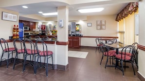 A hotel dining area with a kitchen in the background, featuring a bar and seating arrangements. - Ramada Hotel & Conference Center by Wyndham Edgewood (Edgewood)