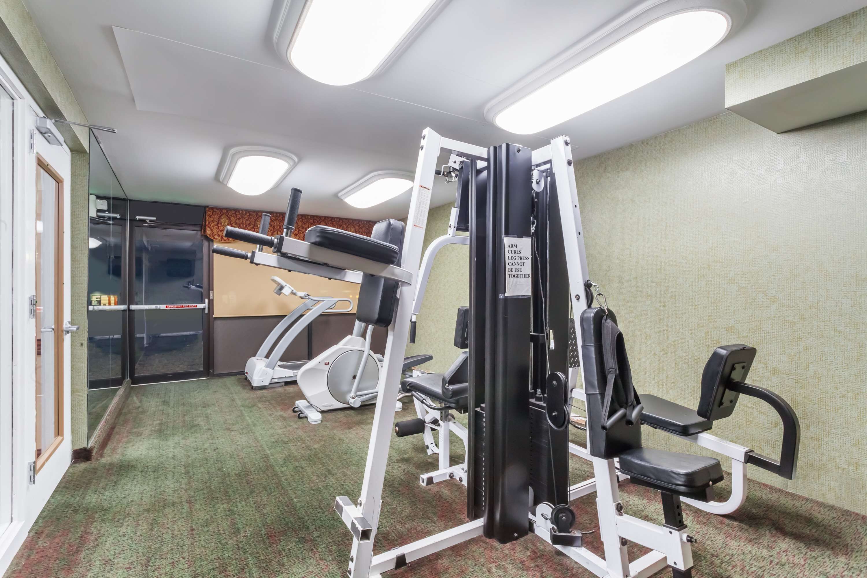 Ein Fitnessstudio mit verschiedenen Trainingsgeräten, einer Spiegelwand und einem Teppichboden.