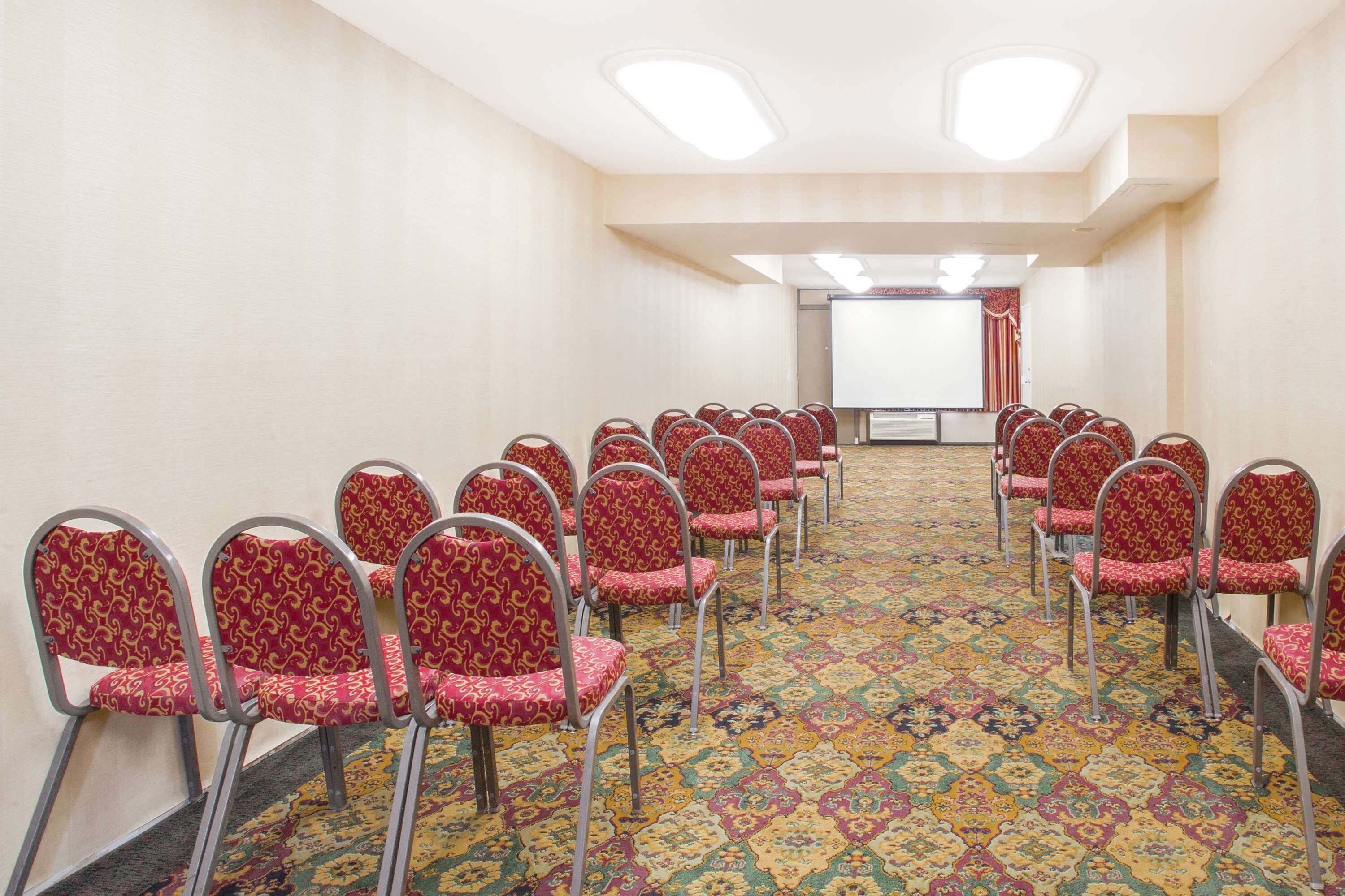 A conference room with rows of red patterned chairs and a carpeted floor.
