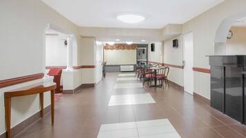 A hotel corridor with a reception desk, a dining area with chairs and tables, and a kitchen area.