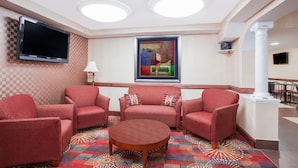 A hotel lobby with a checkered wall, a flat-screen TV, a painting, a patterned carpet, and red upholstered chairs. - Ramada Hotel & Conference Center by Wyndham Edgewood (Edgewood)