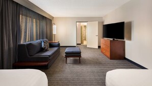 A hotel room with a sofa, ottoman, TV, and a dresser.