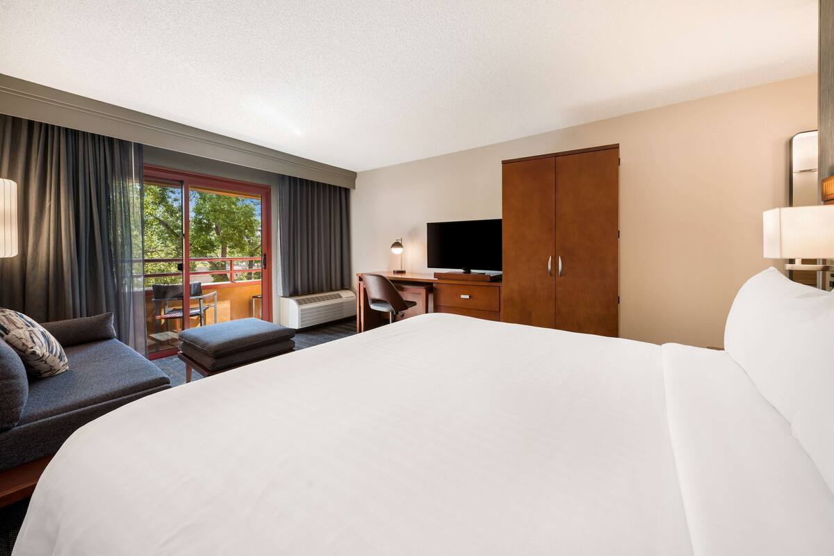 Habitación de hotel con una cama grande, un sofá, un escritorio con televisor y un armario.