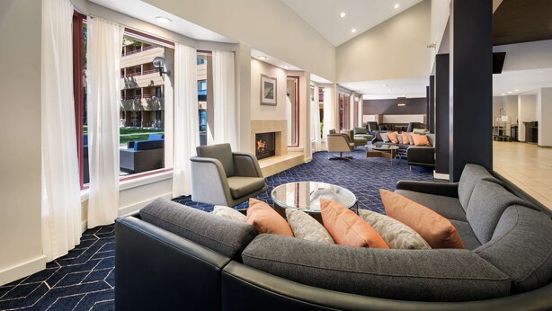 A modern hotel lobby with a curved sofa, a glass coffee table, and a fireplace.