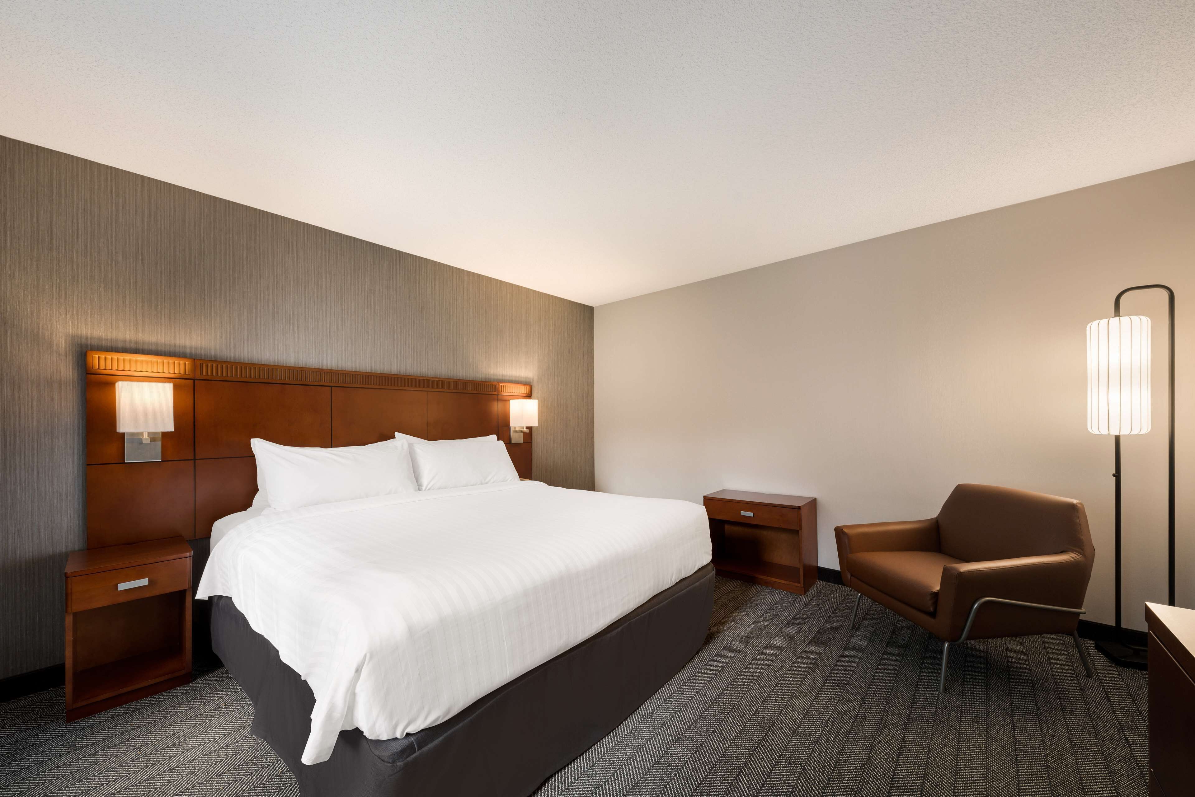 Una habitación de hotel con una cama grande, dos mesitas de noche, una silla y una lámpara de pie.