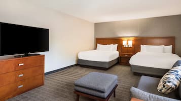 A hotel room with two beds, a television, a wooden dresser, and a small ottoman.
