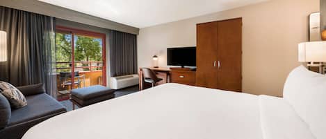 A hotel room with a large bed, a sofa, a desk with a TV, and a wardrobe.