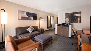 A modern hotel room with a sofa, ottoman, desk, and lamp.