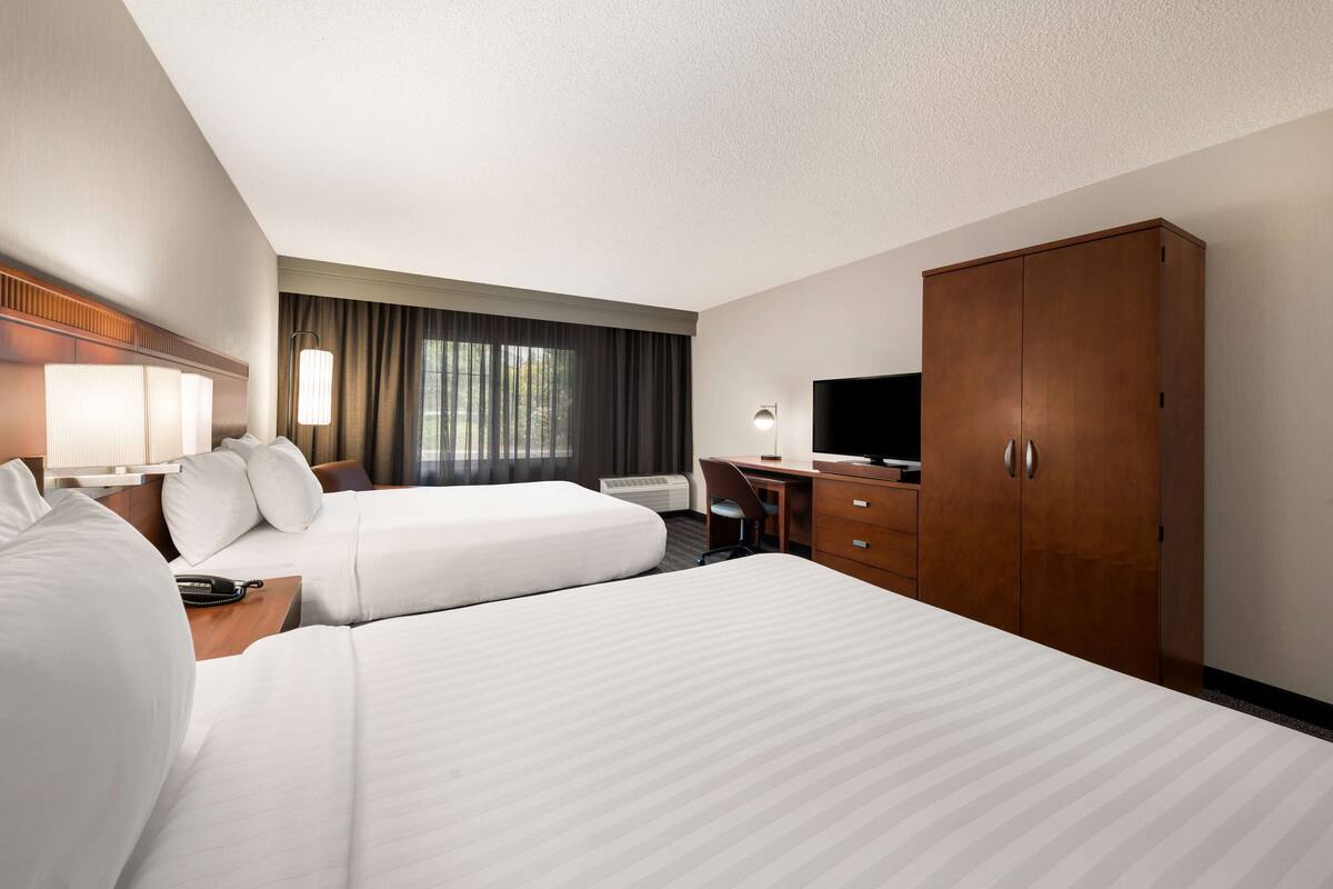 Habitación de hotel con dos camas, un escritorio, un televisor y un armario.