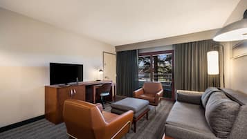 A hotel room with a sofa, two armchairs, a desk with a flat-screen TV, and a lamp.
