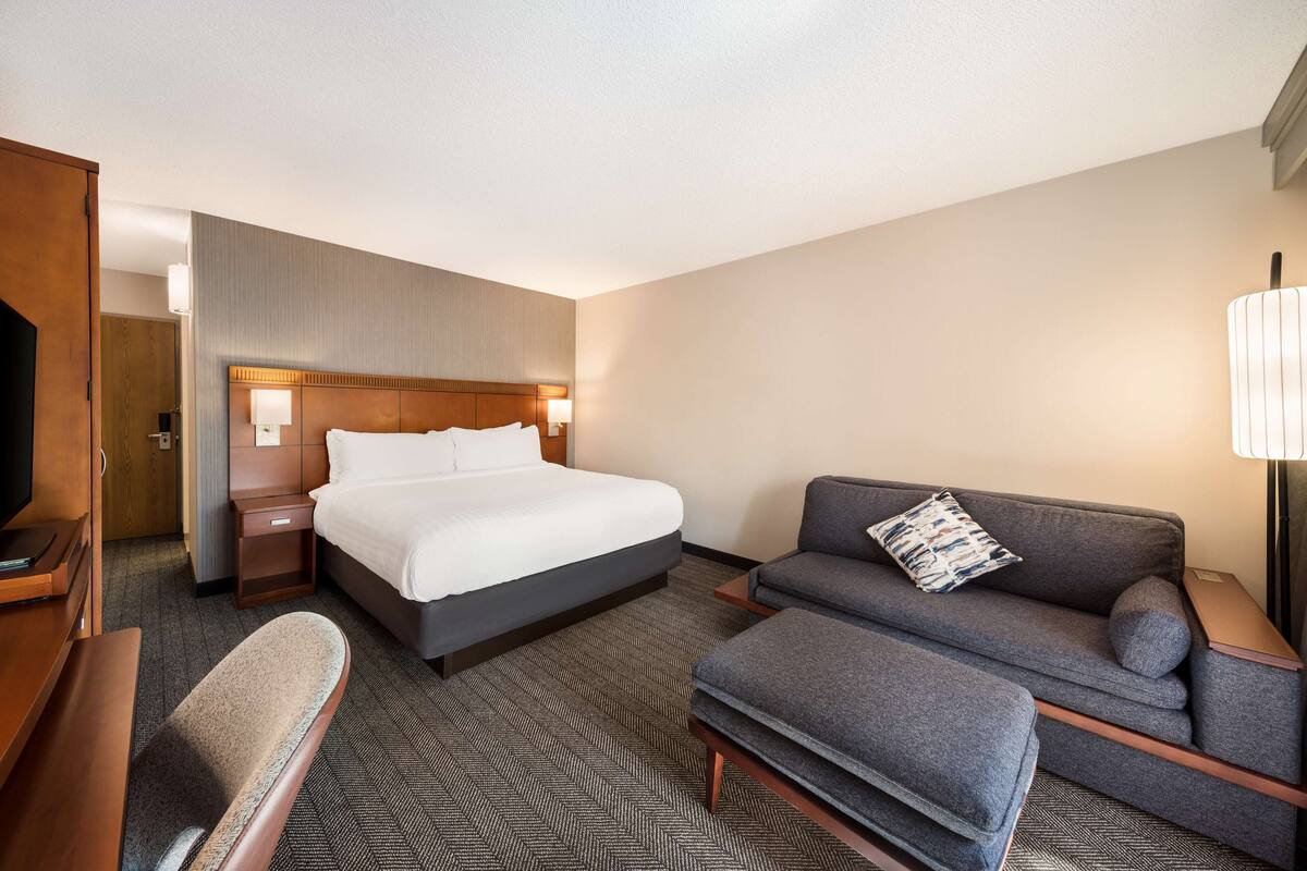 Una habitación de hotel con una cama grande, un sofá, una silla y un televisor.