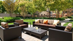 An outdoor patio area with wicker furniture, including sofas and chairs, and a coffee table with a pitcher and glasses.