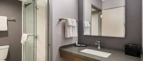 A modern bathroom with a glass-enclosed shower, a sink with a wooden vanity, and a large mirror.