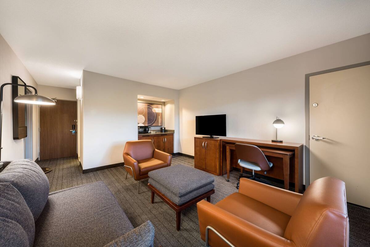 Habitación de hotel con sofá, dos sillones, una mesita, televisión y escritorio con lámpara.