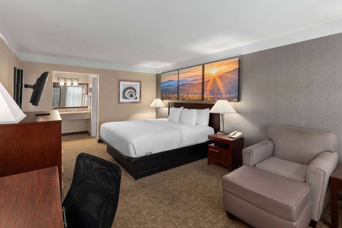 Hotelkamer met een bed, nachtkastjes, een bureau, een stoel en een groot raam met uitzicht op een berglandschap in de zonsondergang.