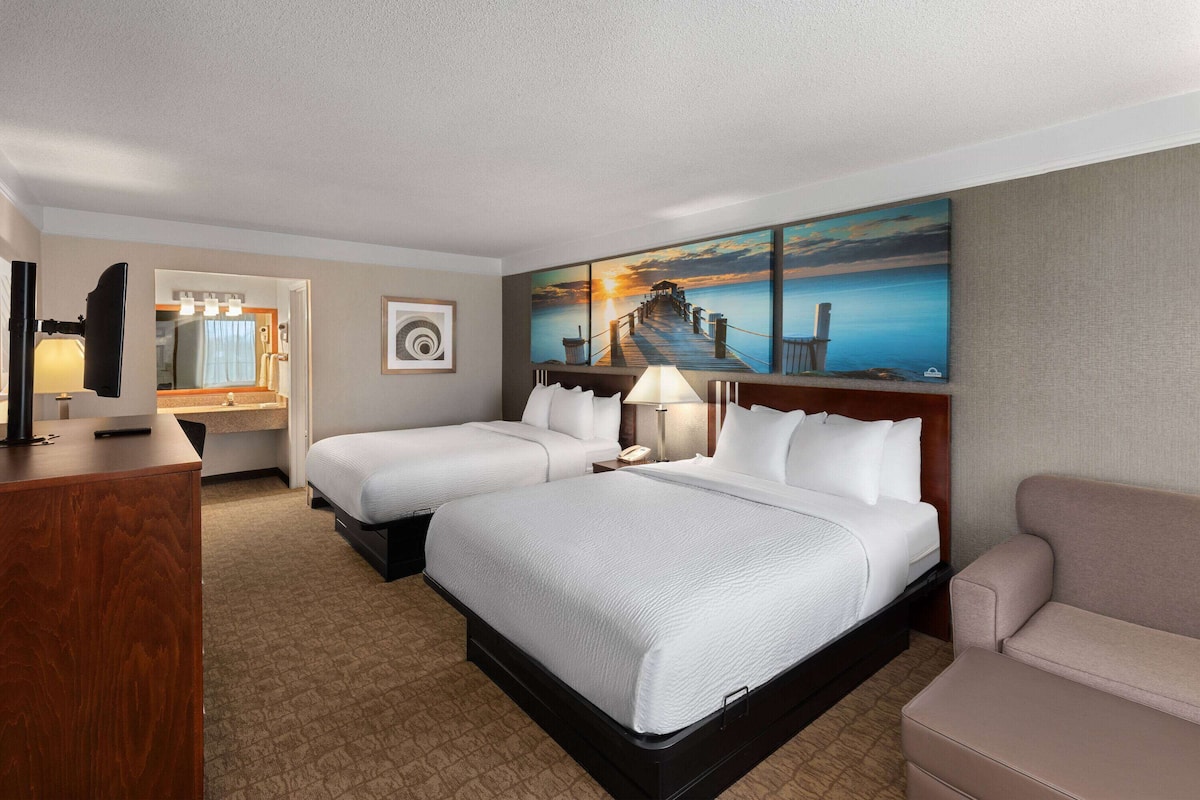 Een hotelkamer met twee bedden, een bureau, een stoel en een schilderij van een pier.