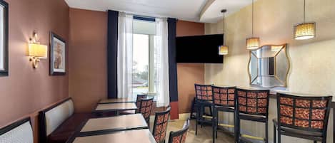 A restaurant with booths and high-top tables, a large window with curtains, and wall-mounted lights.
