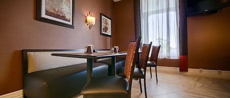 A dining area with a booth, two chairs, a table, and a television on the wall.