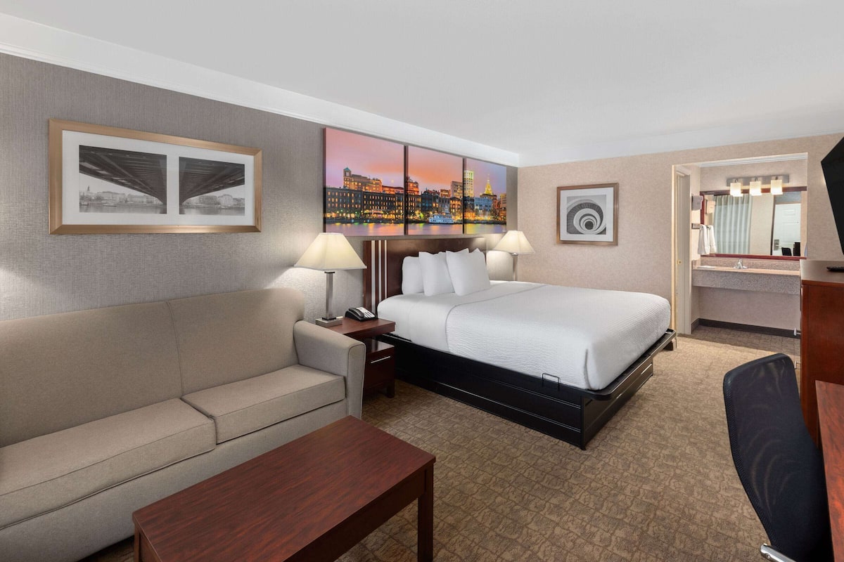 Een hotelkamer met een bed, een bank, een bureau en een stadsgezicht op het doek.