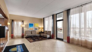 Un vestíbulo de hotel con mostrador de recepción, zona de estar con sofás y una mesa de centro, ventanas amplias con cortinas translúcidas y un tapete 'Days Inn' en el suelo.