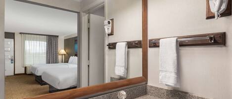 A hotel bathroom with a large mirror, a sink, a towel rack, and a hairdryer mounted on the wall.