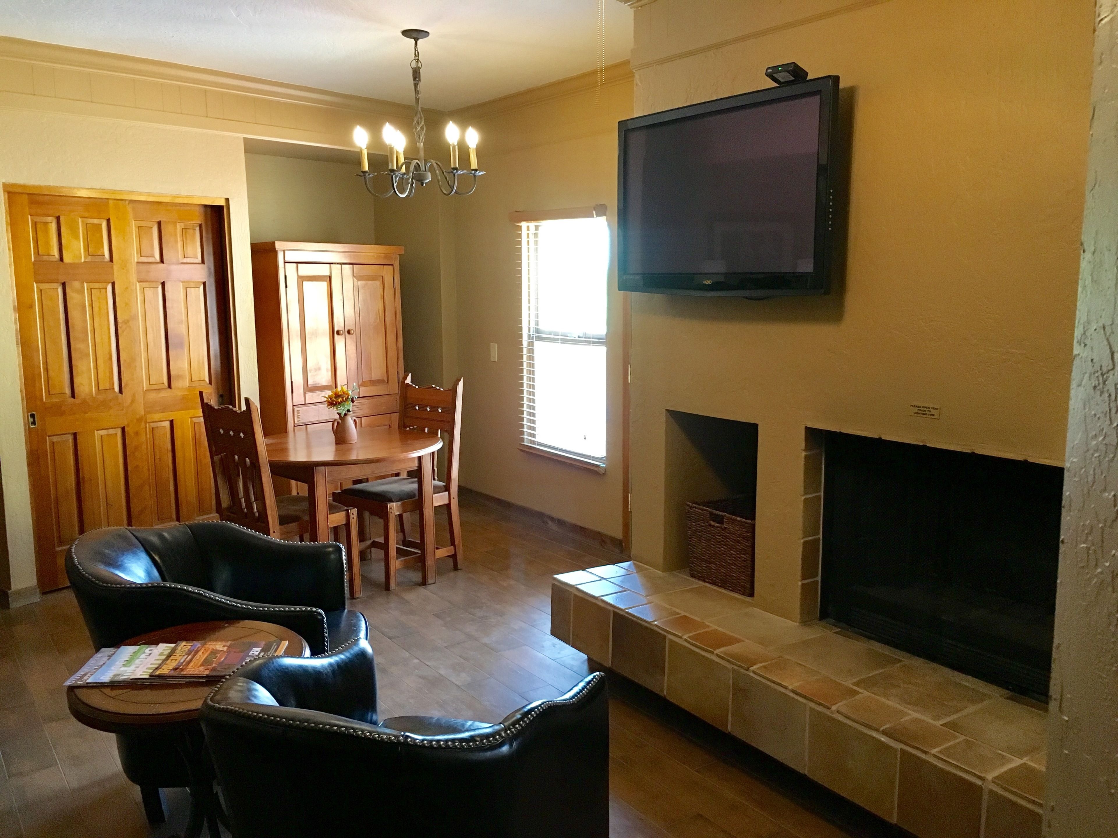 Una sala de estar con chimenea, un televisor colocado encima, una mesa de comedor con sillas y una araña.
