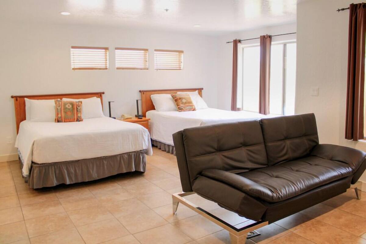 A hotel room with two beds, a brown leather sofa, and a window with curtains.