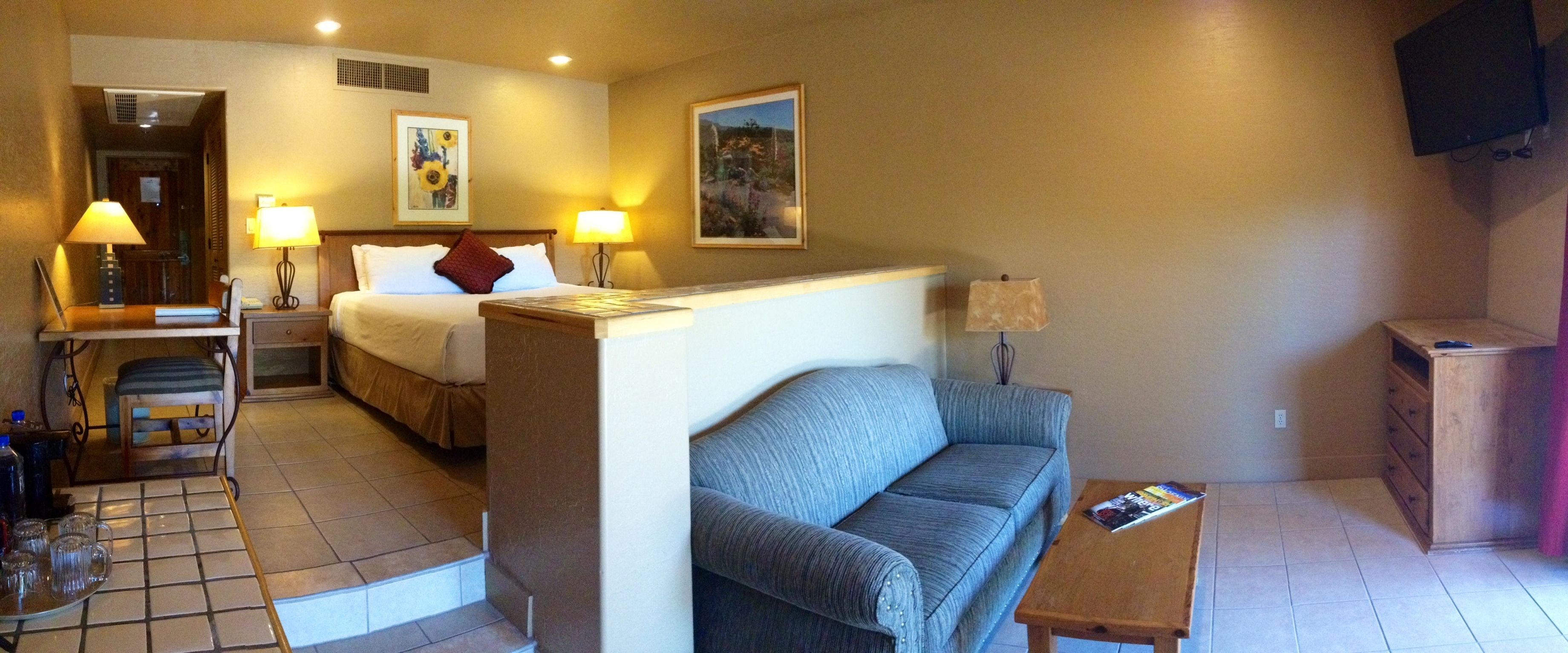 Une chambre d’hôtel avec un lit, un canapé, une petite table, une télévision et un bureau avec une lampe.