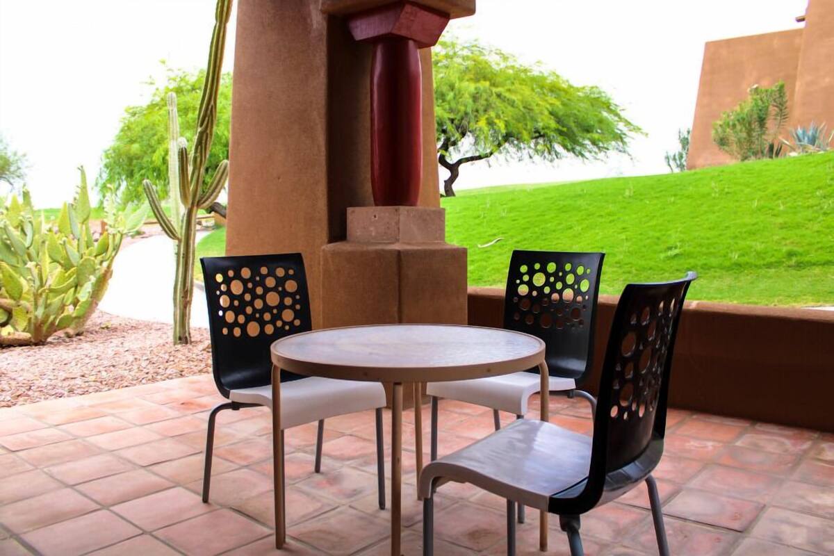 A patio with a round table and four chairs, surrounded by a cactus garden and a view of a green lawn.