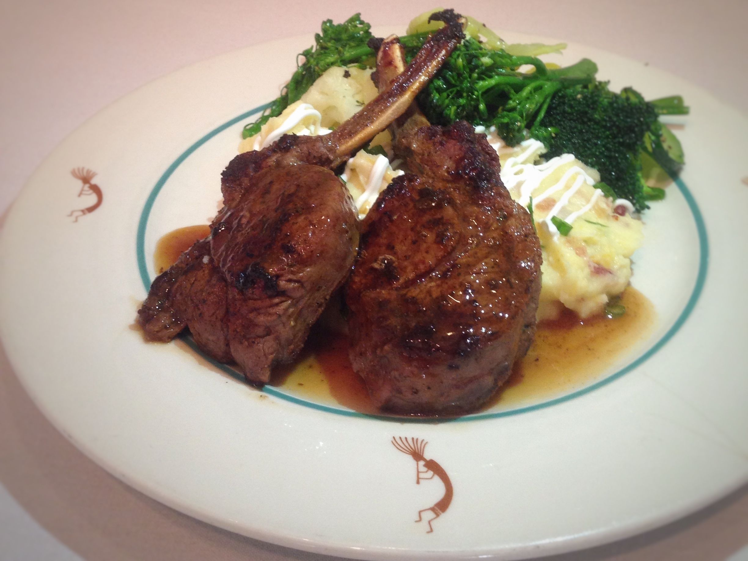 A plate of food with two lamb chops, broccoli, and mashed potatoes.