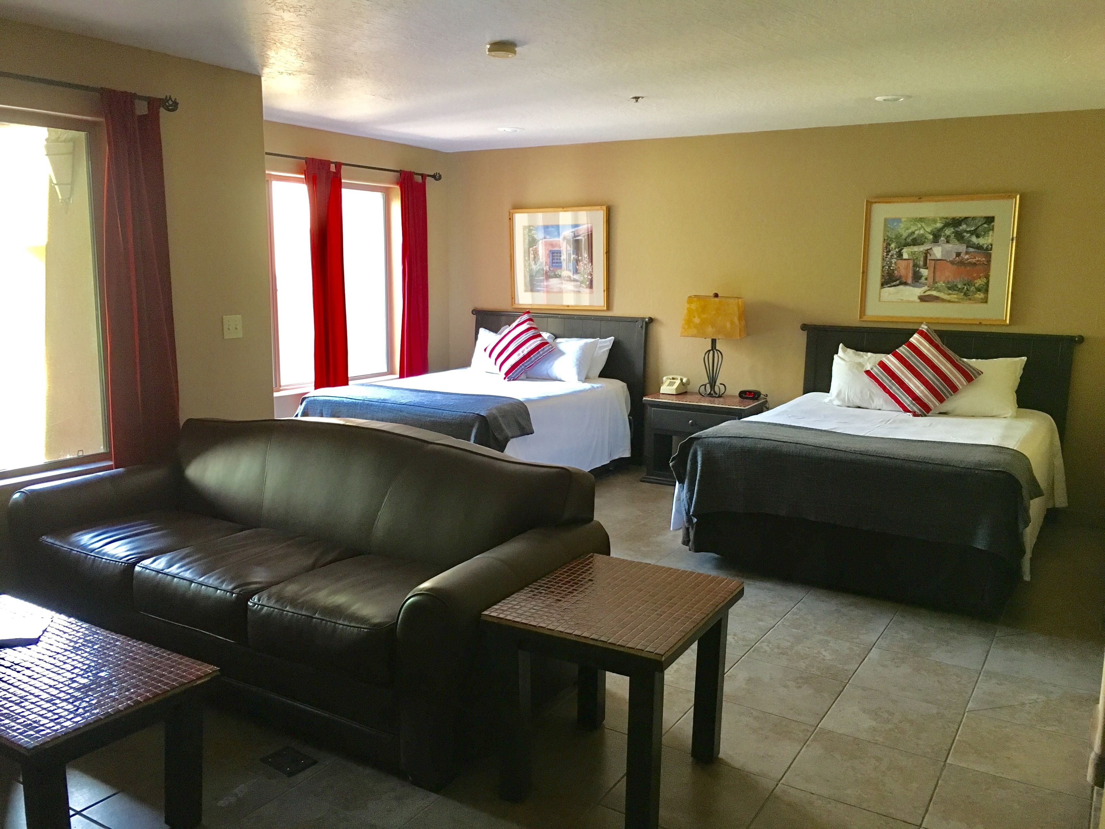 Habitación de hotel con dos camas, un sofá de cuero, una mesita pequeña y una mesita de noche con lámpara.