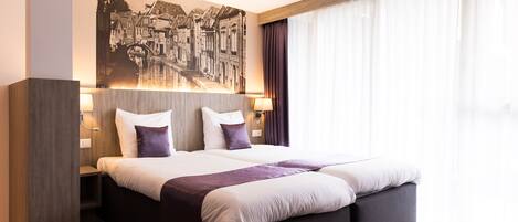 A modern hotel room with a large bed, a cityscape artwork on the wall, and a large window with curtains.