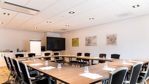 Un salón de conferencias con una larga mesa, sillas, un televisor y obras de arte en las paredes.