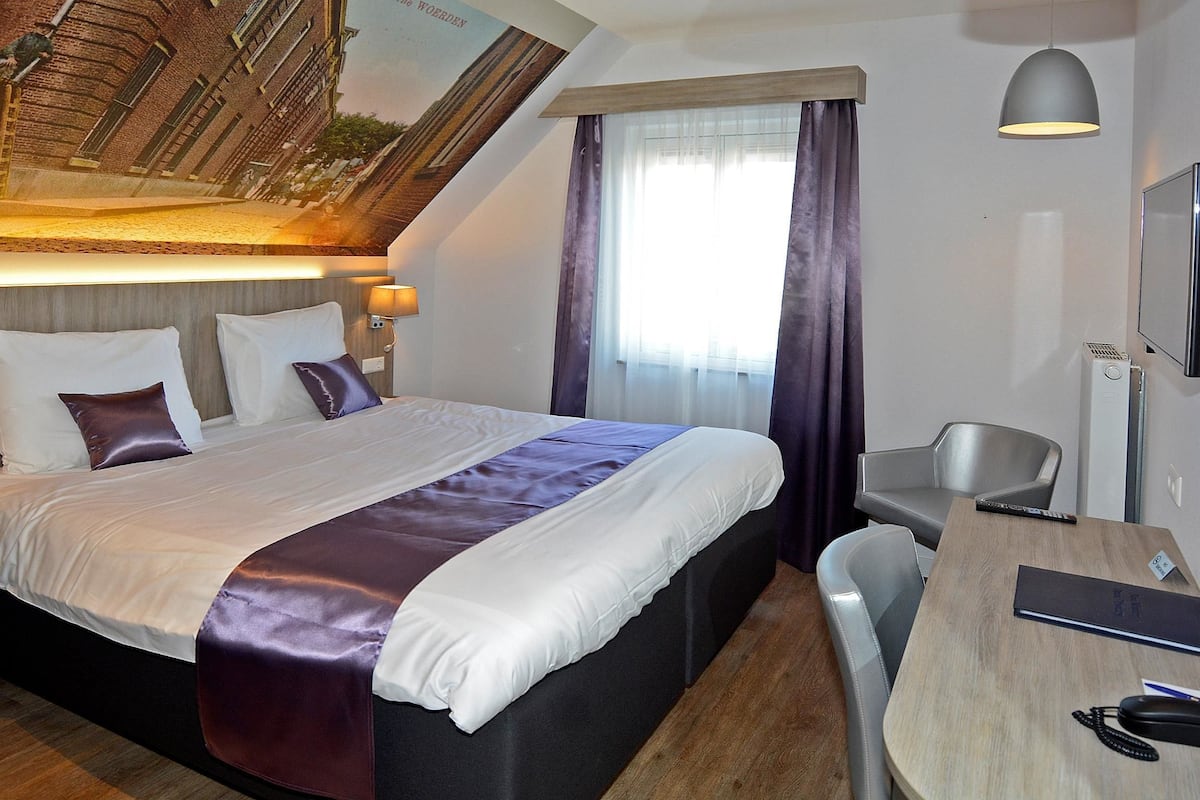 Une chambre d’hôtel avec un grand lit, un bureau, une chaise, une télévision et une fresque au plafond.