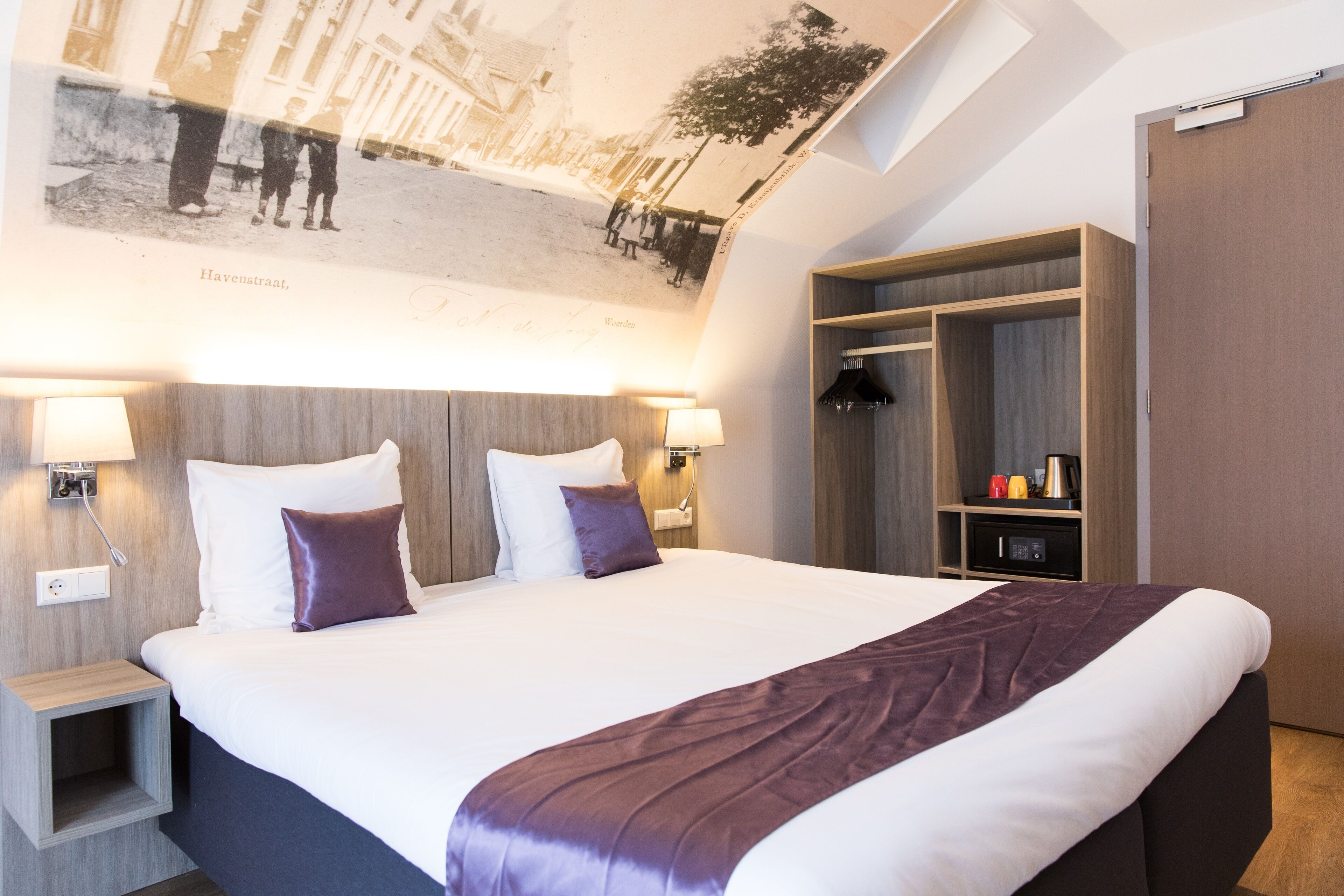 A modern hotel room with a large bed, two bedside lamps, a wardrobe, and a ceiling mural.