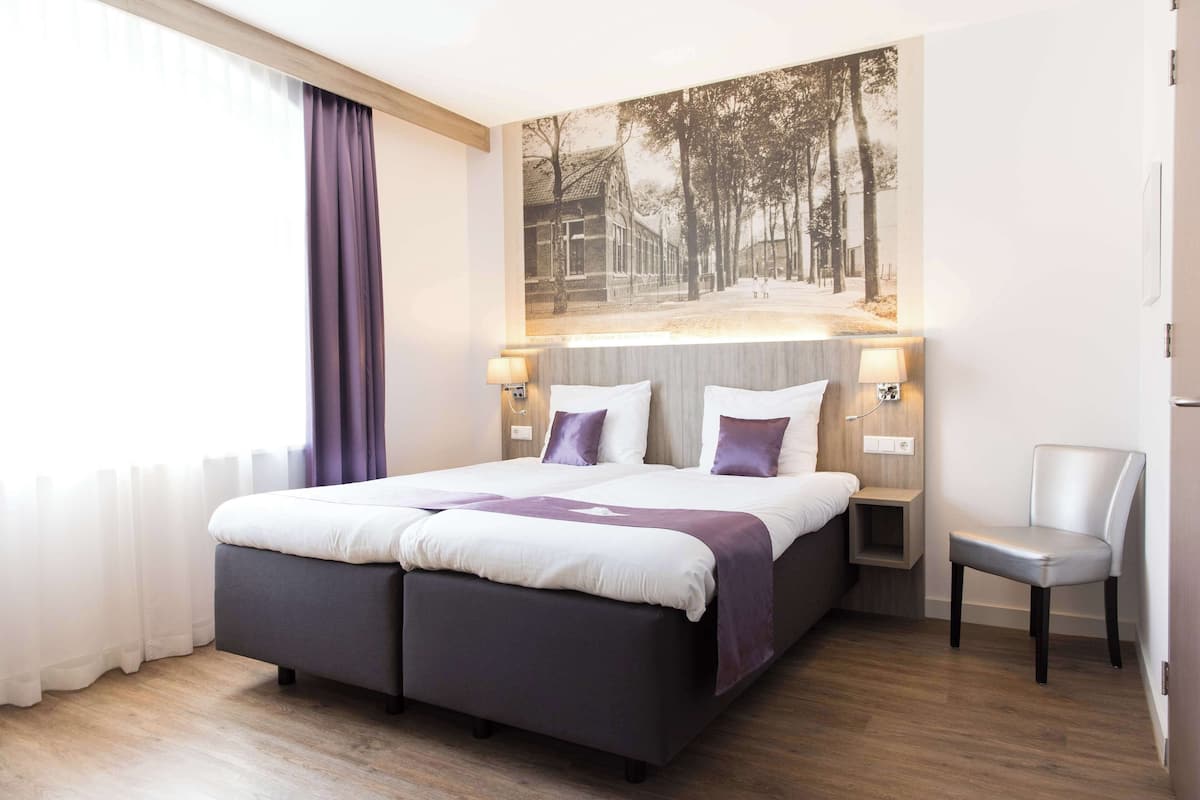 Une chambre d’hôtel moderne avec un grand lit, une chaise et un tableau accroché au mur.