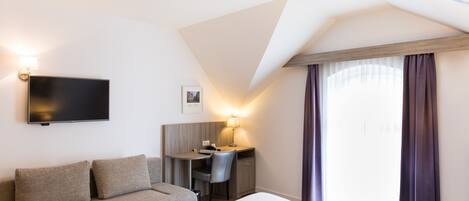 A hotel room with a bed, a desk, a chair, a flat-screen TV, and a window with curtains.