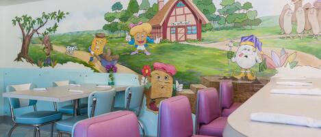 A restaurant with cartoon characters on the wall, purple and blue chairs, and a counter with a waffle sign.