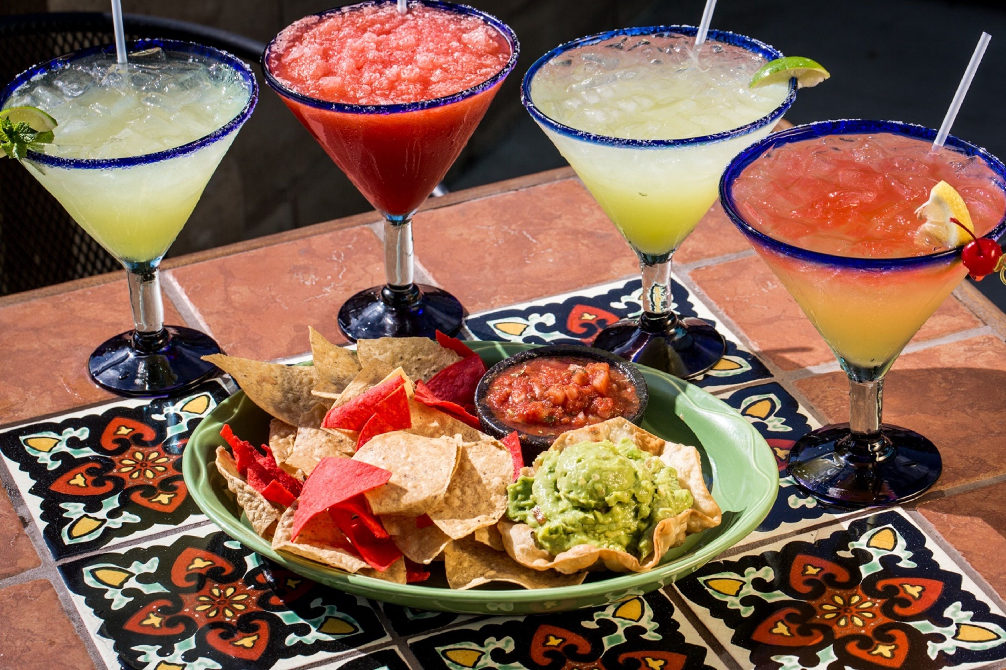 A table with four margaritas, a bowl of guacamole, tortilla chips, and salsa.