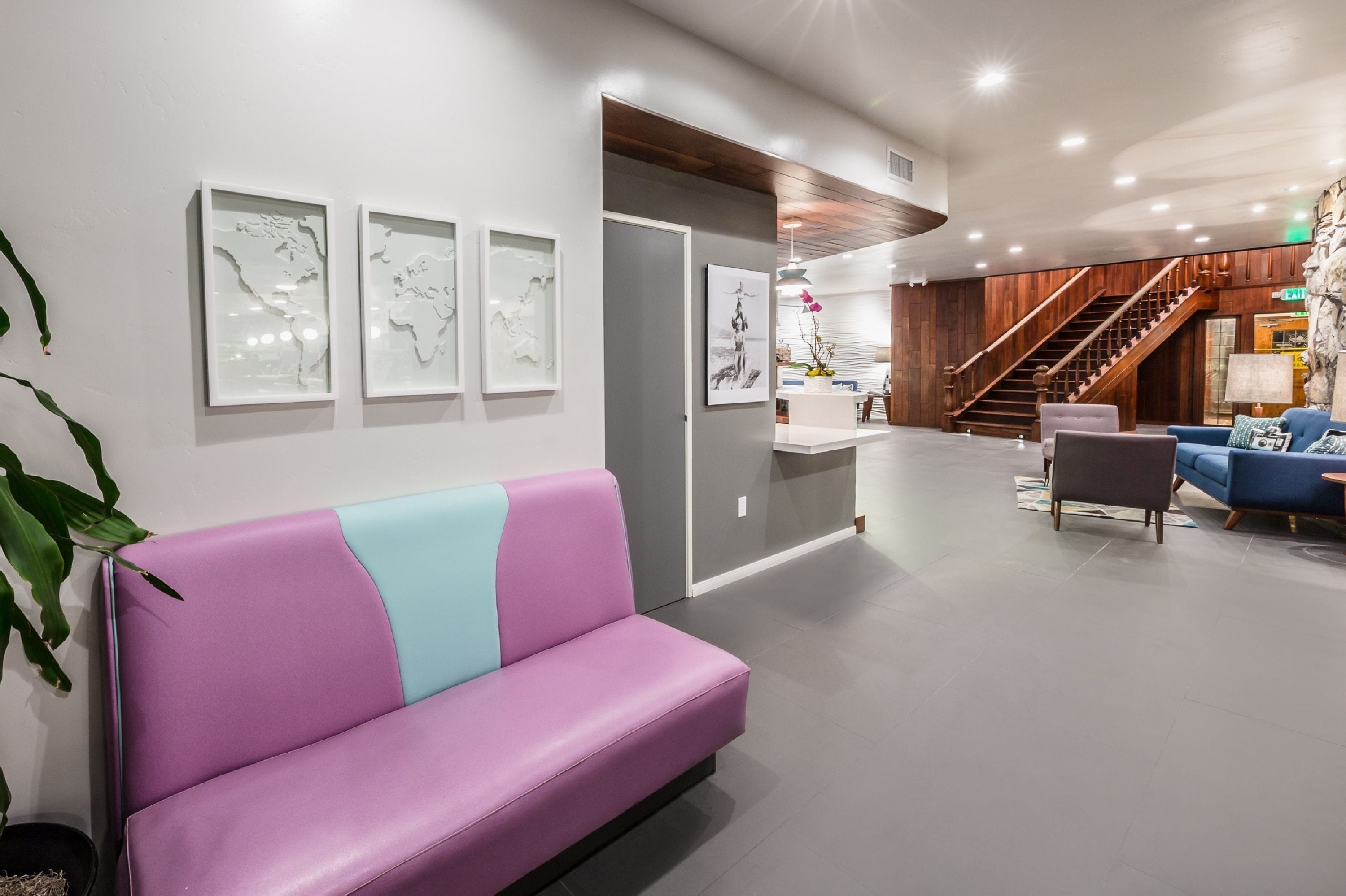 Un vestíbulo moderno con un sofá morado, obras de arte enmarcadas, una escalera y un mostrador de recepción.
