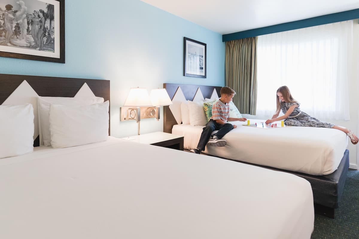 A hotel room with two beds, a nightstand with a lamp, and a framed picture on the wall.