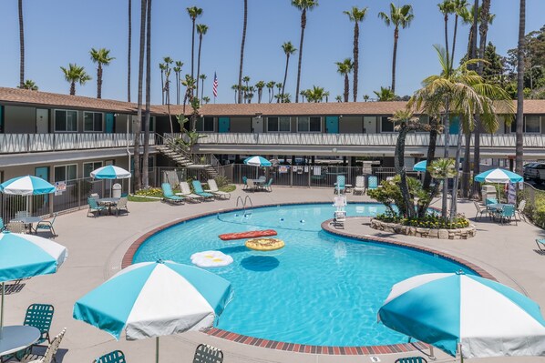 A pool area with lounge chairs and umbrellas, surrounded by palm trees and a building with multiple floors. - Kings Inn San Diego (San Diego)
