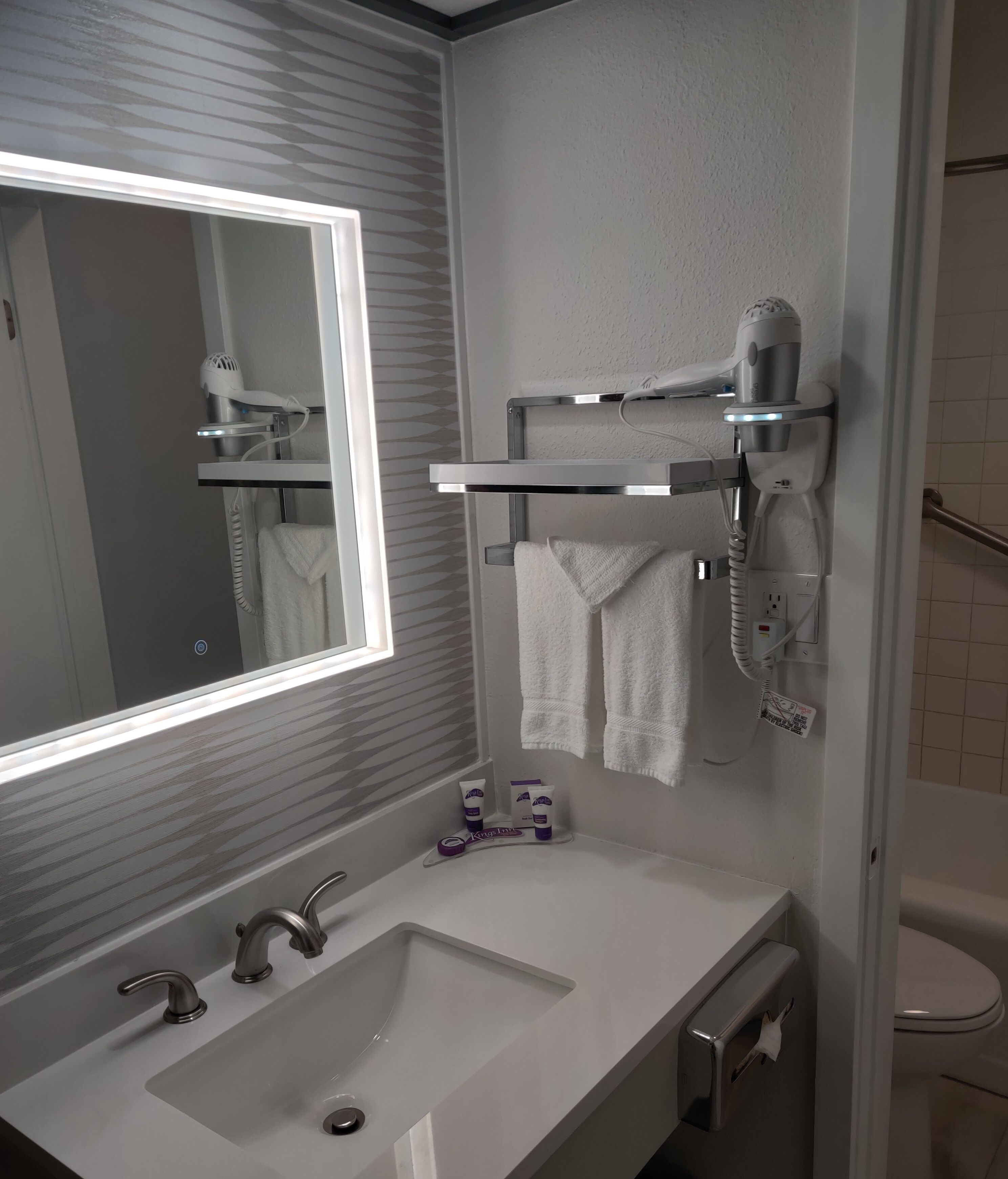 A modern bathroom with a large mirror, a white sink, and a hairdryer mounted on the wall.