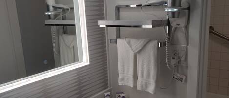 A modern bathroom with a large mirror, a white sink, and a hairdryer mounted on the wall.