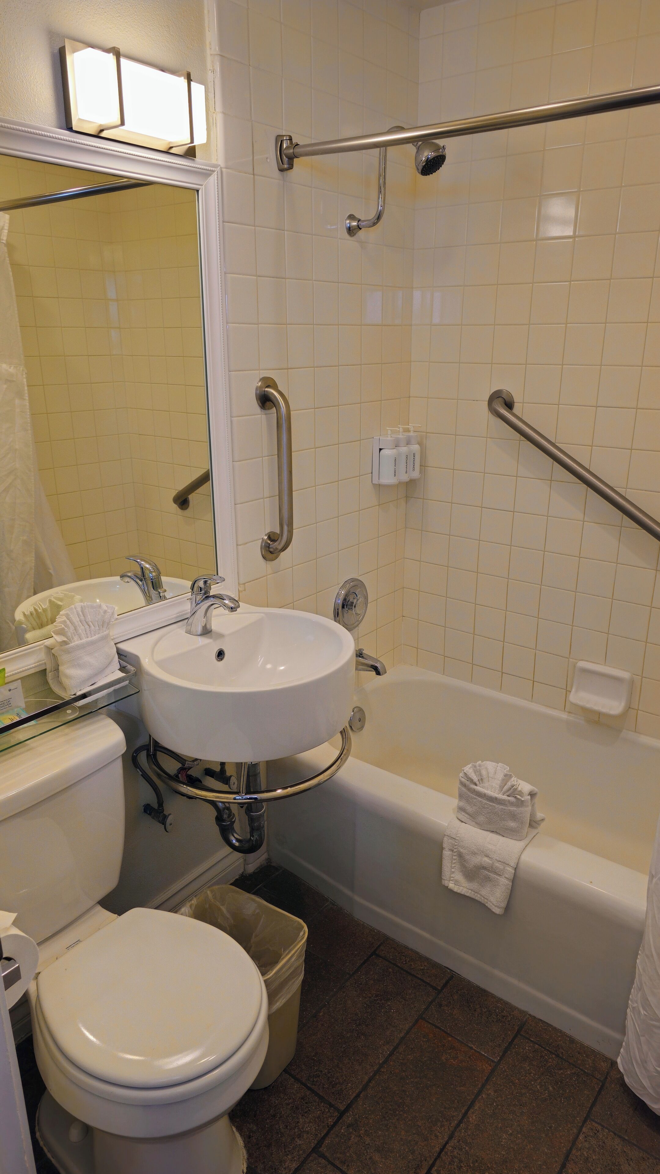 Baño con lavamanos, inodoro y bañera blancos. Cuenta con barras de apoyo para mayor seguridad.