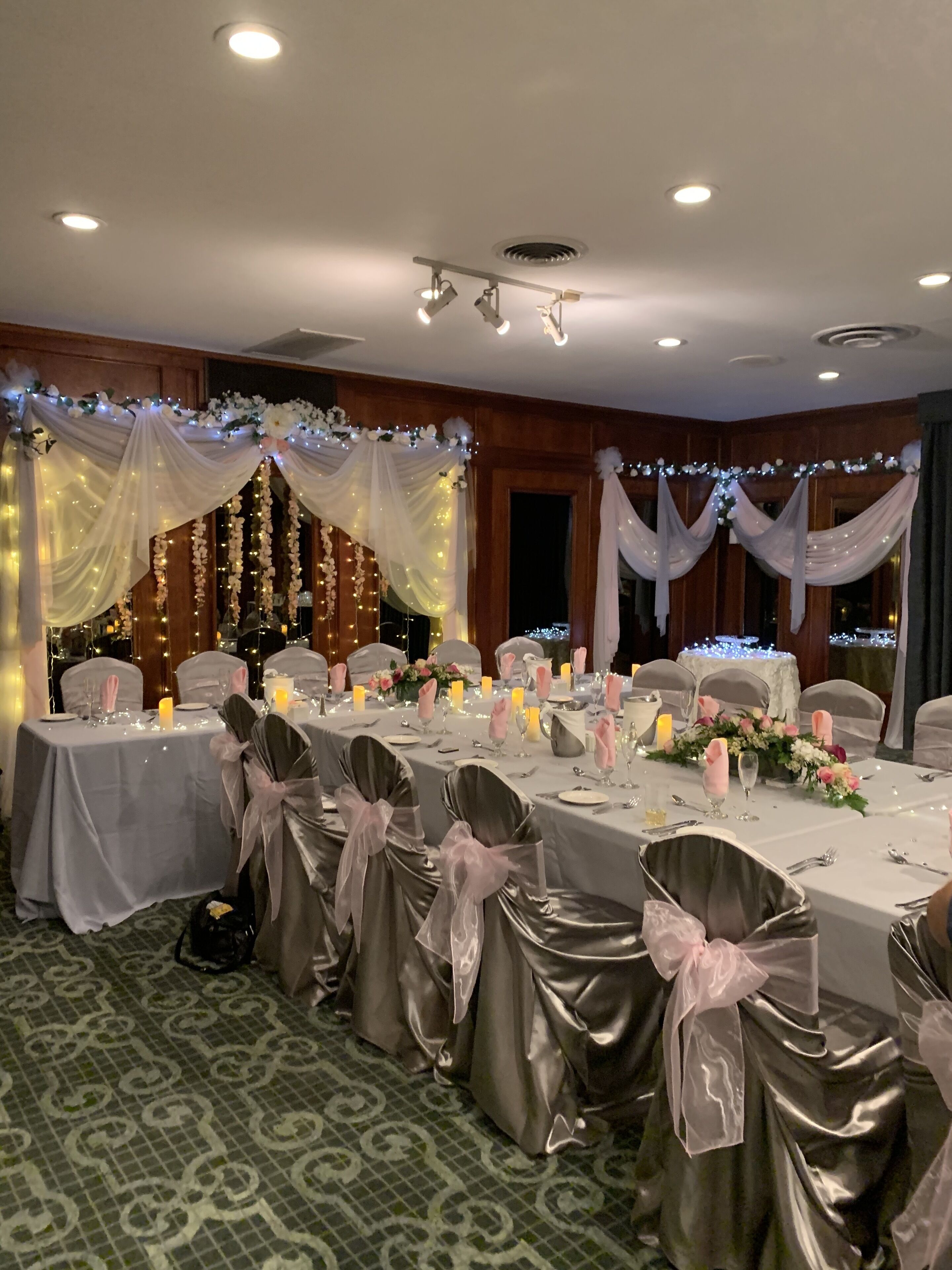 Un salón de banquetes con mesas dispuestas para un evento formal, con cortinas y arreglos florales.