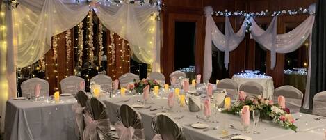 Un salón de banquetes con mesas dispuestas para un evento formal, con cortinas y arreglos florales.