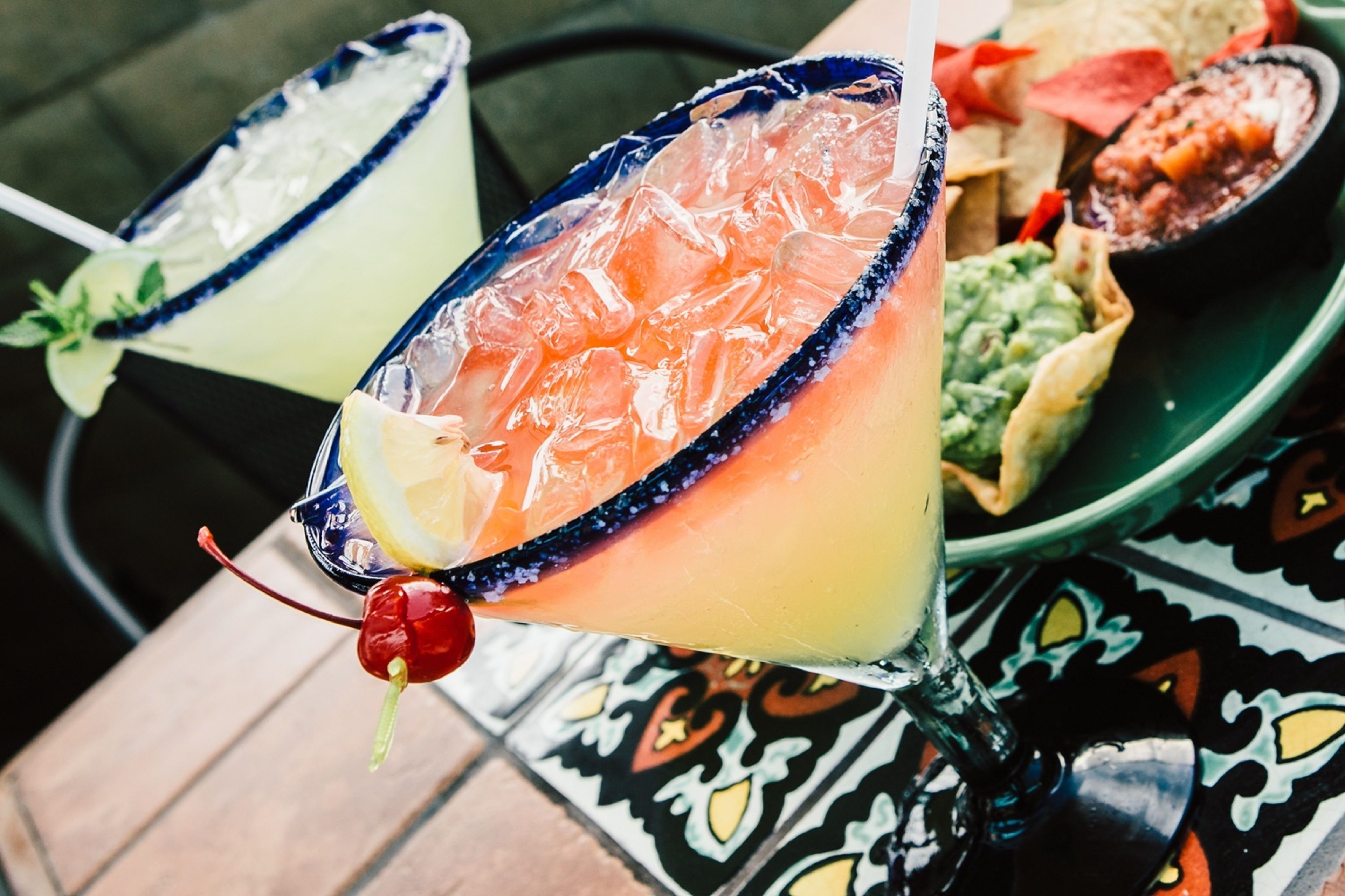 Zwei Margaritas mit Limetten- und Kirschgarnitur auf einem Tisch mit gemustertem Tischläufer.