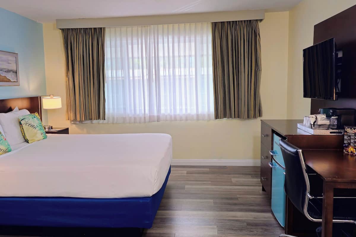 A hotel room with a bed, a desk, a television, and a window with curtains.