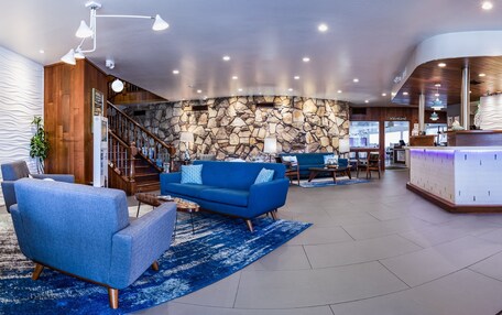 A modern lobby with a stone wall, blue sofas, a reception desk, and a staircase.